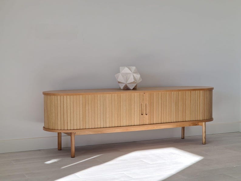 May include: A light wood cabinet with two doors and a geometric white sculpture on top. The cabinet has a rounded top and sits on four legs.