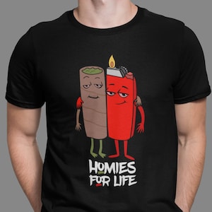 Puede incluir: Camiseta negra con una ilustración de dibujos animados de un porro y un encendedor abrazándose. El texto "Homies For Life" está impreso debajo de la ilustración.