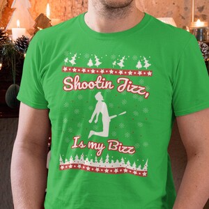 May include: A green t-shirt featuring a white silhouette of a person shooting a basketball. The text "Shootin Jizz, Is my Bizz" is printed in red on the shirt.