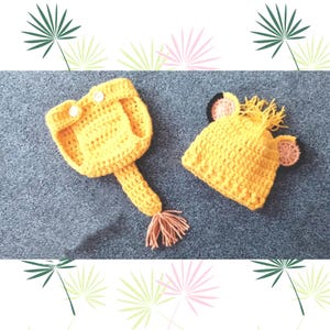 Op de afbeelding: Een geel gebreid leeuwenkostuum voor een baby, bestaande uit een muts met oren en een aparte jumpsuit met een staart.