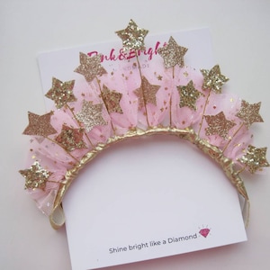 May include: A gold glitter star headband with pink tulle and gold wire. The headband has the text "Pink & Bright" on a white card.
