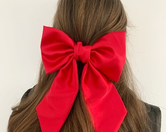 May include: A large, bright red satin bow hair clip. The bow is tied in a classic shape with two long tails.