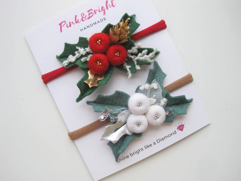 May include: Two elastic headbands on a white display card labeled Pink & Bright Handmade and Shine bright like a Diamond. One headband features red felt berries and green leaves, the other has white felt berries and green leaves.