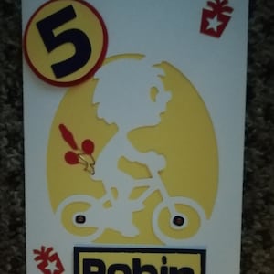 Eine wunderschöne handgemachte Karte im Format 18x18 mit einem geschnittenen Kind auf einem Fahrrad. Name und Alter zu Ihrer Spezifikation hinzugefügt.