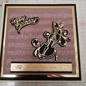 Luxury  large music card featuring a violin in black and gold on a background of a musical score, featuring the sentiment Happy birthday.