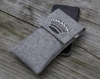 May include: A grey felt phone case with a sparkly crown design. The case is designed to fit a smartphone.