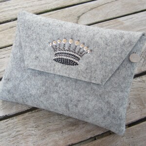 Op de afbeelding: Een grijze wollen clutch met een zilveren kroonversiering en een zilveren label met de tekst "No. 14".