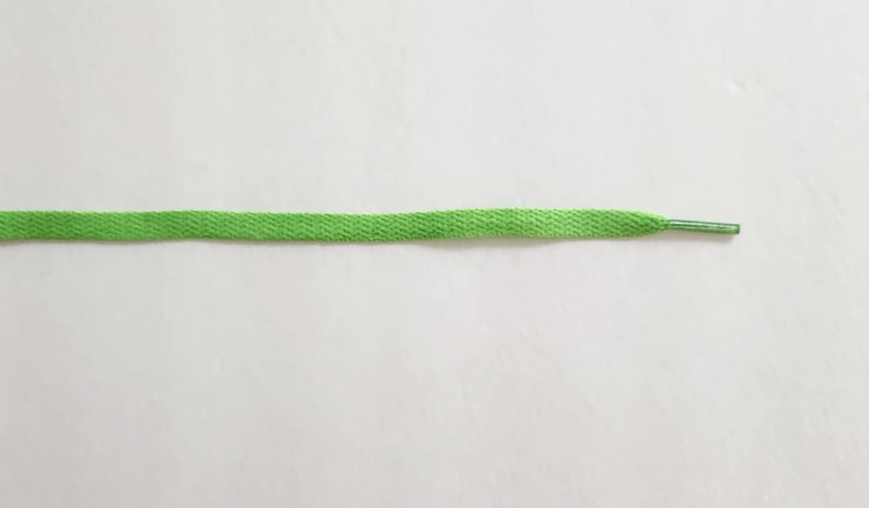 Puede incluir: Un cord&oacute;n de zapato verde brillante sobre un fondo blanco.