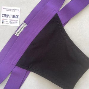 Puede incluir: Ropa interior morada y negra con tirantes ajustables. La ropa interior tiene el texto "Strip It Back" en una etiqueta blanca.