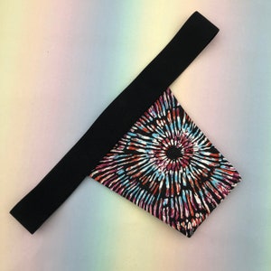 May include: Black fabric with a colorful tie-dye pattern. The fabric is shaped like a triangle with a black strap.