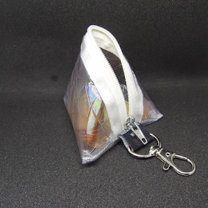 Può includere: Una piccola borsa a zip trasparente e iridescente con una cerniera bianca e un portachiavi argentato.
