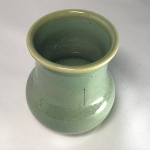 May include: A green ceramic vase with a rounded body and a slightly flared rim. The vase has a light green glaze with a subtle sheen.