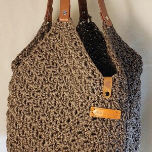 May include: A brown crocheted tote bag with leather straps and a brown leather label that says "JGS ORIGINS".