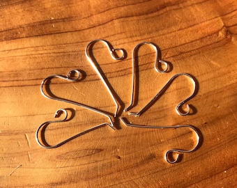 May include: A set of six silver ornament hooks, arranged in a starburst pattern on a wooden surface.