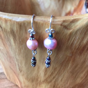 May include: A pair of dangle earrings with pink pearl beads and iridescent black beads hanging from silver hooks.