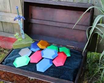 May include: A wooden treasure chest with a blue velvet lining is open and filled with colorful, hexagonal, plastic gems. A plastic sword with a blue handle and a green blade is on a green base outside the chest.