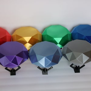 May include: Seven colorful, faceted, geometric shapes resembling gemstones, each mounted on a black stand. The colors are red, gold, green, blue, purple, gray, and light blue.