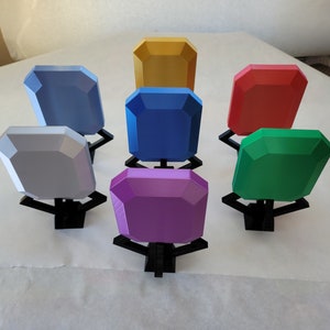 May include: Seven colorful gemstone-shaped objects on black stands. The colors are gold, light blue, blue, red, green, and purple.