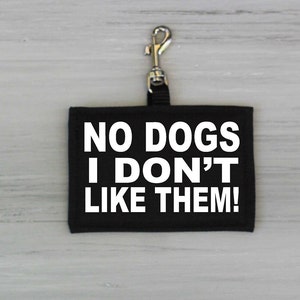 May include: Black fabric dog tag with white text that reads "NO DOGS I DON'T LIKE THEM!" The tag has a silver metal clip.