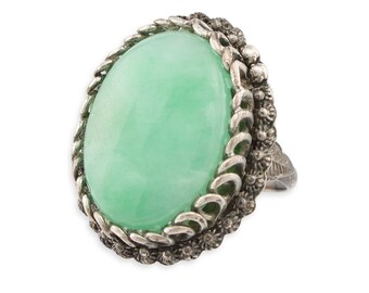 May include: A silver ring with a large oval green jade stone set in a detailed silver filigree design.