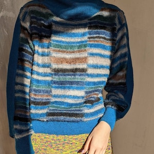 May include: A blue and grey striped sweater with a high neck and long sleeves. The sweater is made of a soft, fuzzy material.
