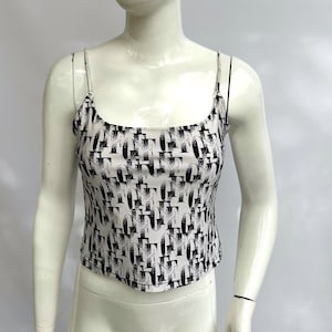 Puede incluir: Un top blanco de tirantes con un patrón geométrico en blanco y negro. El top tiene tirantes finos y un escote redondo.