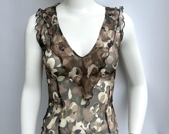 May include: A sleeveless top with a V-neck and a floral pattern in shades of brown, beige, and black. The top has a sheer fabric and is trimmed with a black ruffle along the neckline and armholes. The garment is displayed on a mannequin.