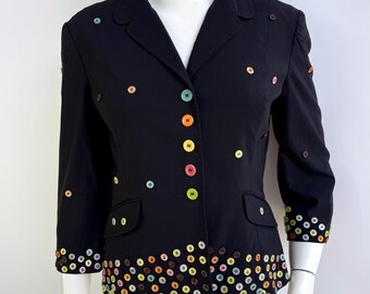 May include: Black blazer with colorful button embellishments. The blazer features a classic collar, three-quarter sleeves, and a row of buttons down the front. The buttons are in various colors, including yellow, pink, green, and orange.