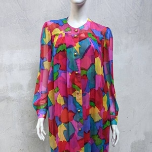 May include: A long-sleeved, sheer dress with a colorful abstract print. The dress has a button-up front and a loose, flowing silhouette.