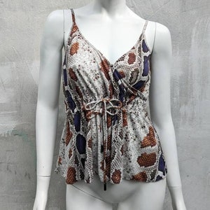 Op de afbeelding: Een wit, mouwloos topje met een slangenhuidprint in tinten bruin, wit en paars. Het topje heeft een trekkoord in de taille.