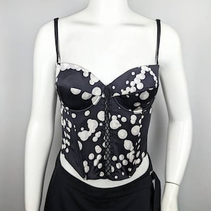 May include: A black and white polka dot corset with a lace-up front. The corset has a sweetheart neckline and adjustable straps.