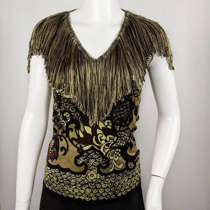 May include: A black and gold top with a fringe neckline and a patterned design. The pattern features a stylized floral design with a dragon-like creature.