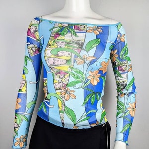 May include: A blue, green, and orange long-sleeved mesh top with a floral and comic book print. The top has an off-the-shoulder neckline.