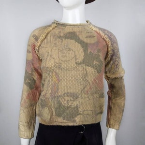 May include: A beige sweater with a colorful abstract print. The sweater has a crew neck and long sleeves.