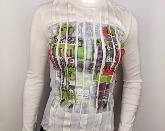 May include: White long-sleeved shirt with vertical pleats and a graphic print of colourful magazine clippings. The print includes the text "FACT" and "1000".