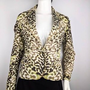 Może przedstawiać: Zielony i brązowy wzorzysty blazer z jednym guzikiem. Blazer ma wycięty kołnierz i długie rękawy.