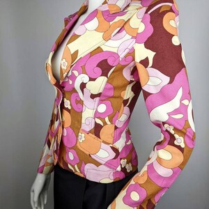 May include: A pink, brown, and orange patterned blazer with a button closure. The blazer has a fitted silhouette and long sleeves.