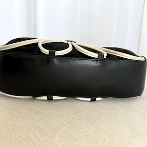 Puede incluir: Un bolso negro con una base de cuero liso y una secci&oacute;n superior adornada con una serie de bucles circulares blancos. El bolso tiene una silueta estructurada y redondeada con un dise&ntilde;o limpio y un acabado negro s&oacute;lido en el panel inferior.