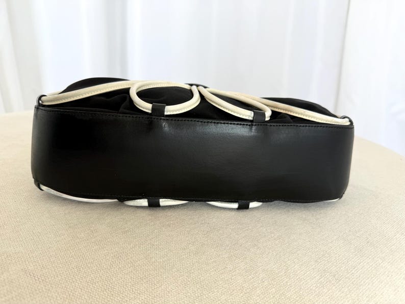 Puede incluir: Un bolso negro con una base de cuero liso y una secci&oacute;n superior adornada con una serie de bucles circulares blancos. El bolso tiene una silueta estructurada y redondeada con un dise&ntilde;o limpio y un acabado negro s&oacute;lido en el panel inferior.