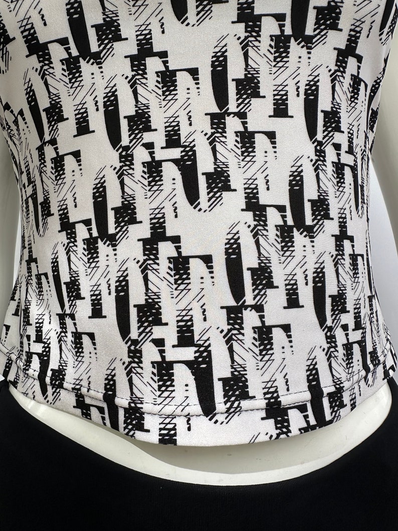 May include: White top with a black and white abstract print. The print features a repeating pattern of letters.