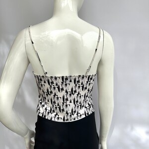 May include: White tank top with a black and white geometric pattern. The tank top has thin straps and a cropped fit.