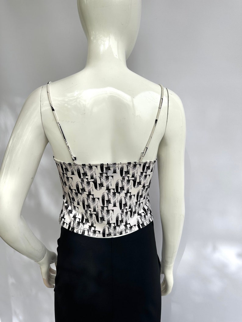 May include: White tank top with a black and white geometric pattern. The tank top has thin straps and a cropped fit.