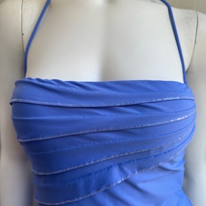 Pu&ograve; includere: Un abito a fascia blu pervinca con corpetto a strati. L'abito presenta un design senza spalline con cinturino all'americana ed &egrave; impreziosito da paillettes argentate lungo le cuciture a strati. L'abito &egrave; esposto su un manichino.
