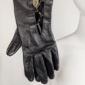 May include: Black leather gloves with a lace-up detail on the back of the hand. The gloves have a label that reads "ITALY, TALIE, STALE, ITALIN".