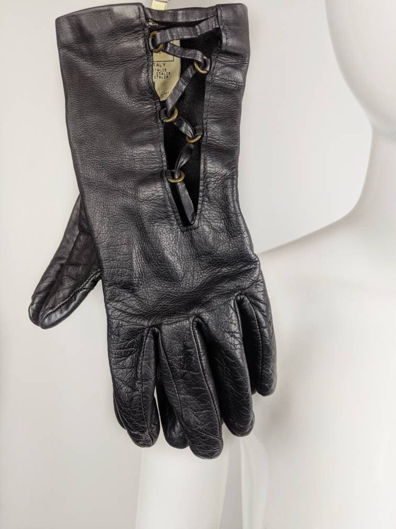 May include: Black leather gloves with a lace-up detail on the back of the hand. The gloves have a label that reads "ITALY, TALIE, STALE, ITALIN".