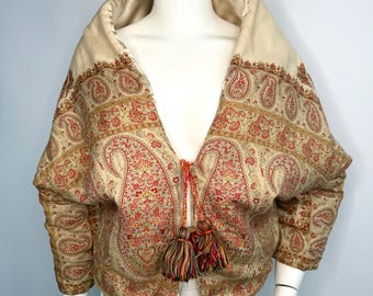 May include: A vintage jacket with a cream-colored collar and a paisley pattern in shades of red, gold, and green. The jacket has a wide collar and is secured with a tassel tie. The sleeves are three-quarter length.