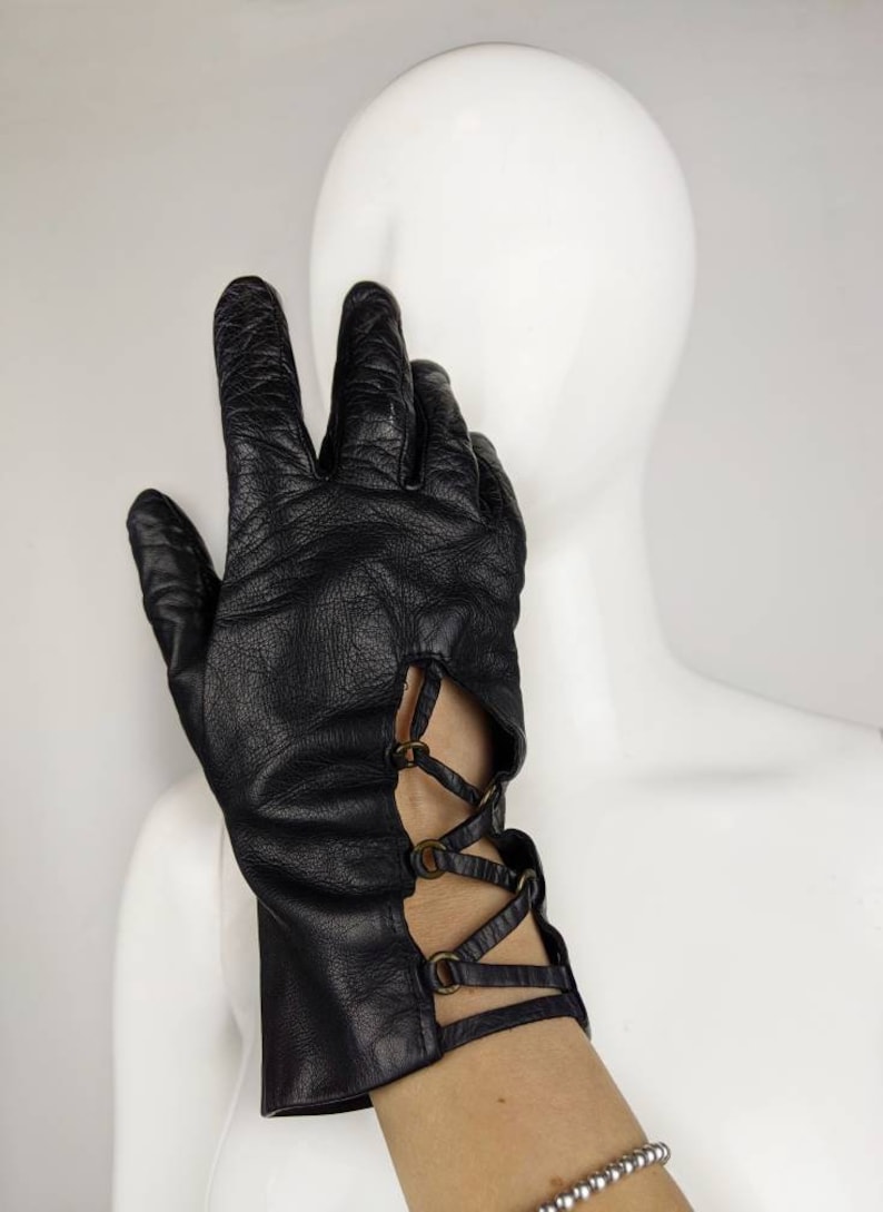 May include: Black leather gloves with a lace-up detail and metal accents on the wrist.