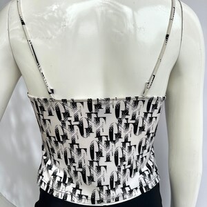 May include: White tank top with a black and white abstract print. The print features a repeating pattern of letters.