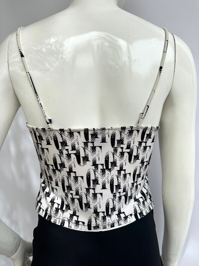 May include: White tank top with a black and white abstract print. The print features a repeating pattern of letters.