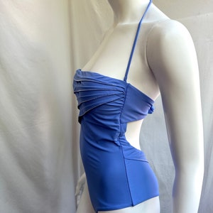 Pu&ograve; includere: Un costume da bagno blu pervinca con collo all'americana e design a taglio. La parte superiore presenta un dettaglio arricciato con un sottile bordo argentato. Il costume intero &egrave; esposto su un manichino.